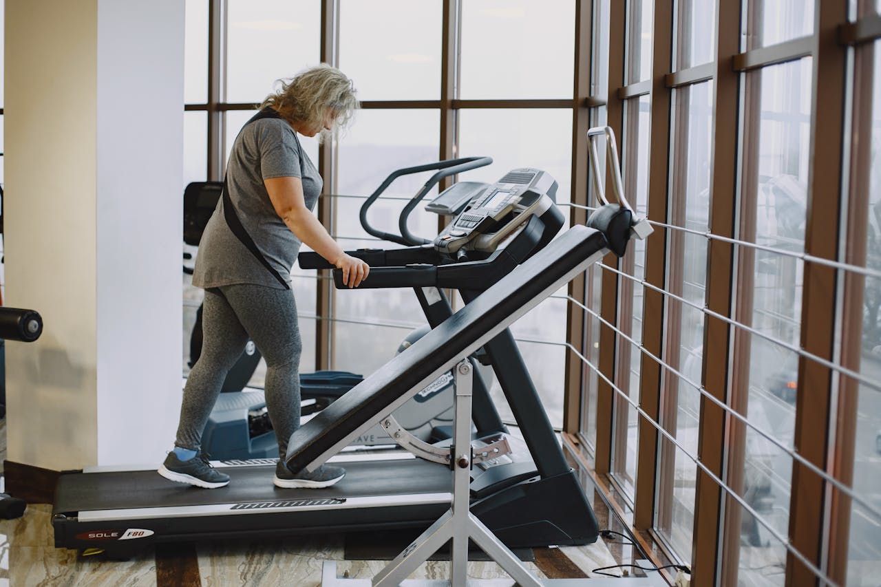 services-02 Adult woman exercising on a treadmill in a bright, modern gym setting.